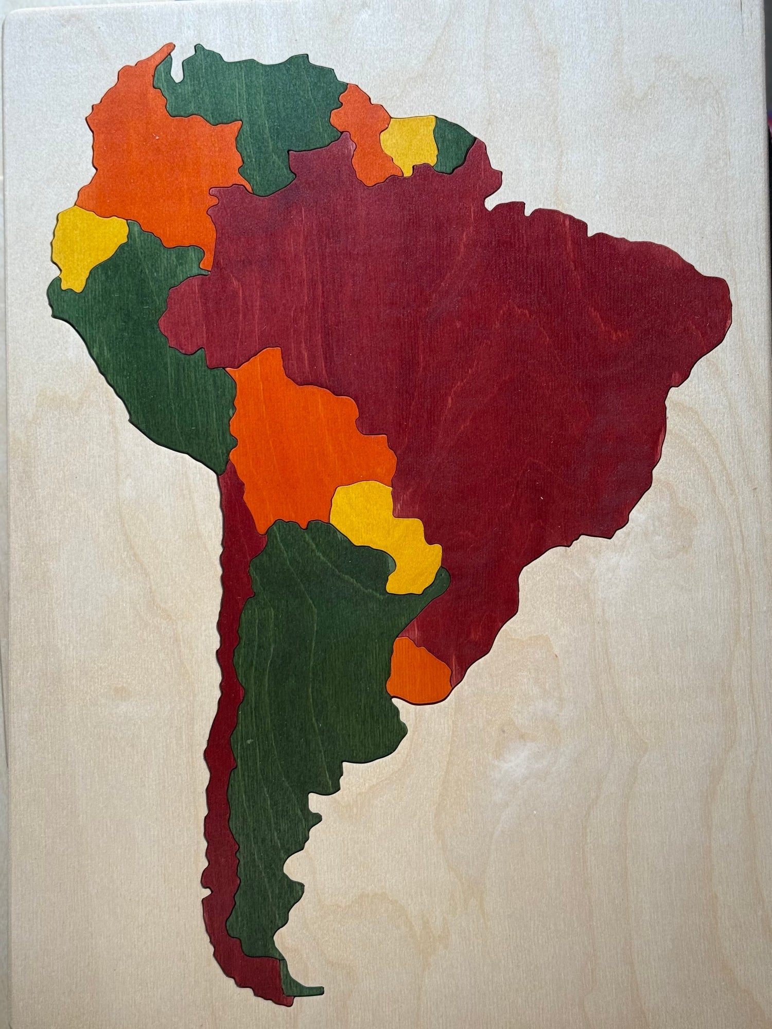 Wooden puzzle in the shape of a map of South America with colored pieces on a wooden base.
