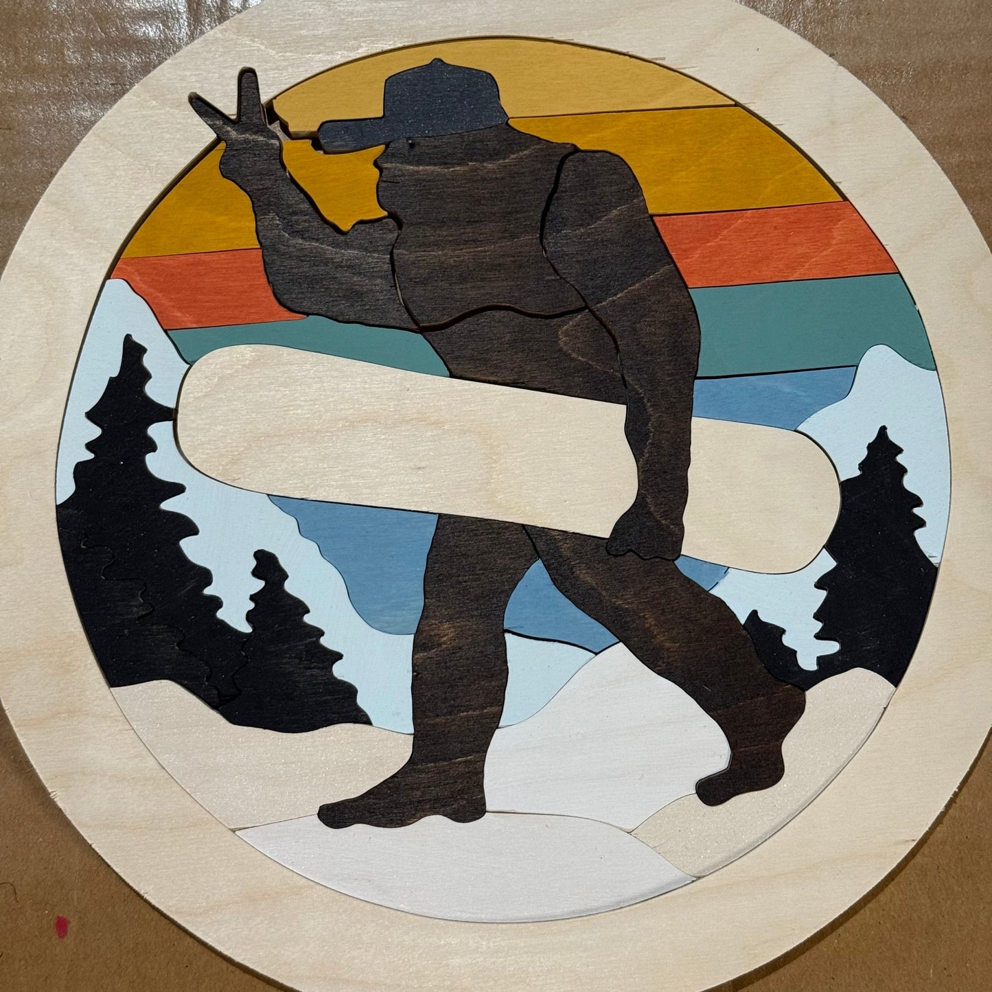 Wooden cutout of a silhouette holding a snowboard with a mountain and sunset background.