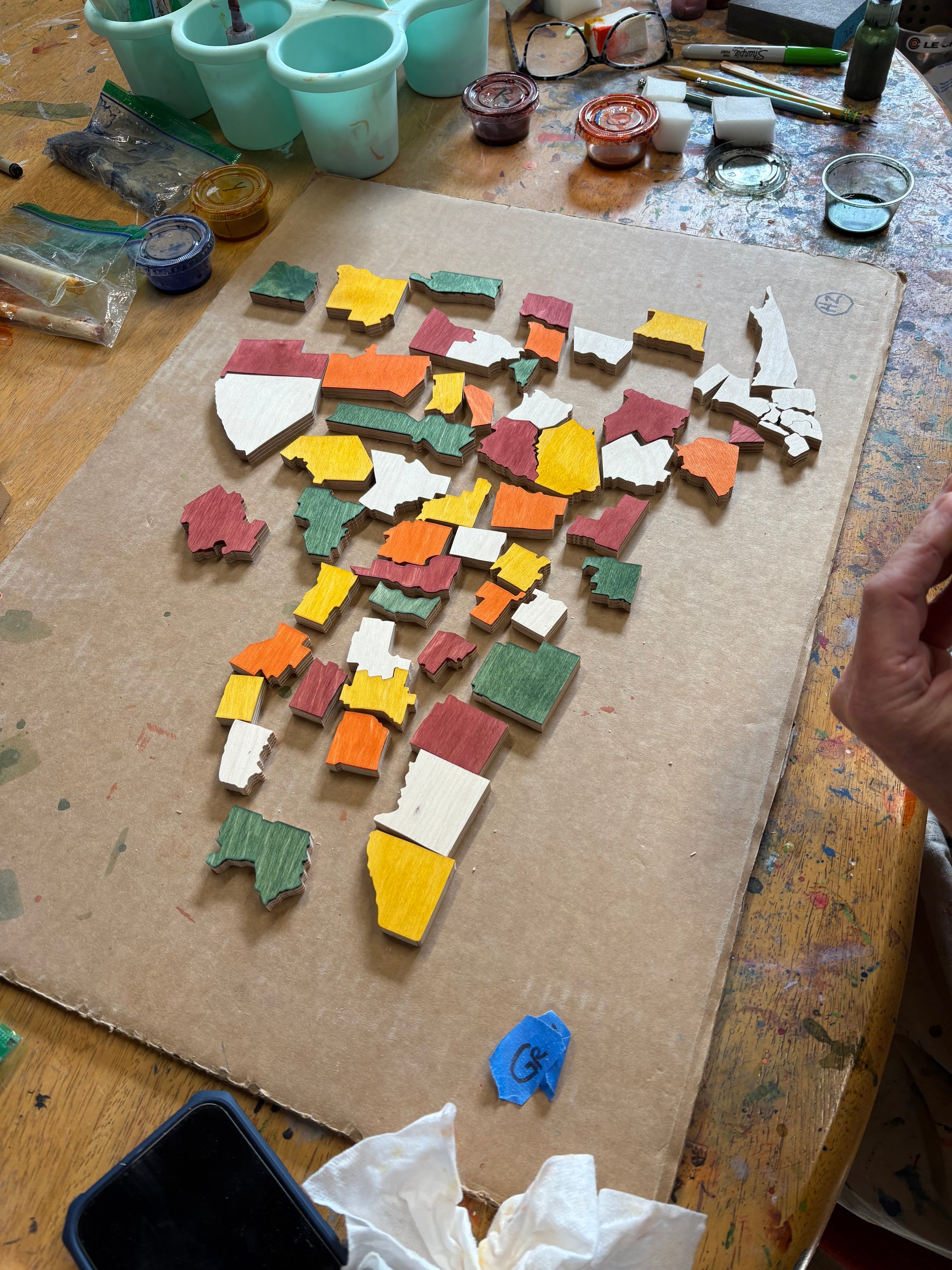 Colorful map of New York puzzle pieces on a cardboard surface with art supplies around.