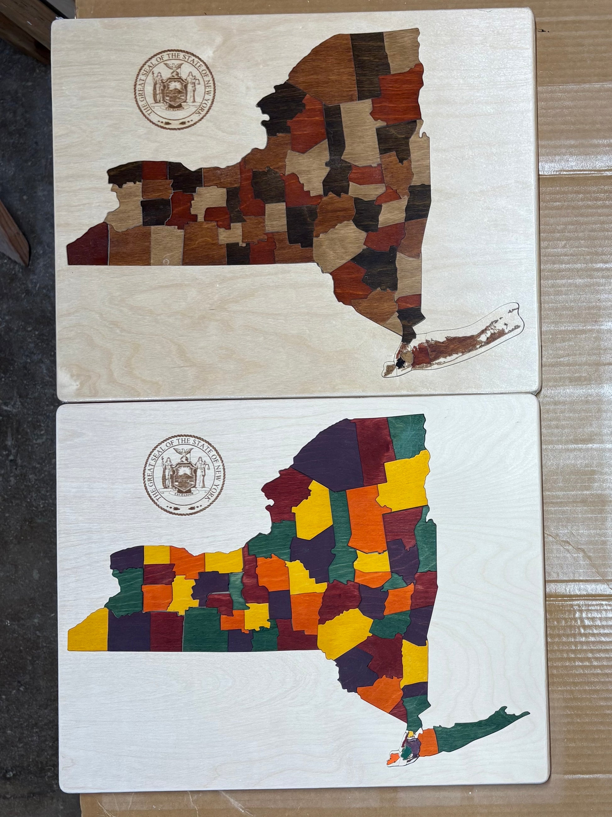 Two wooden puzzles, each shaped like the state of New York with different color palette designs.