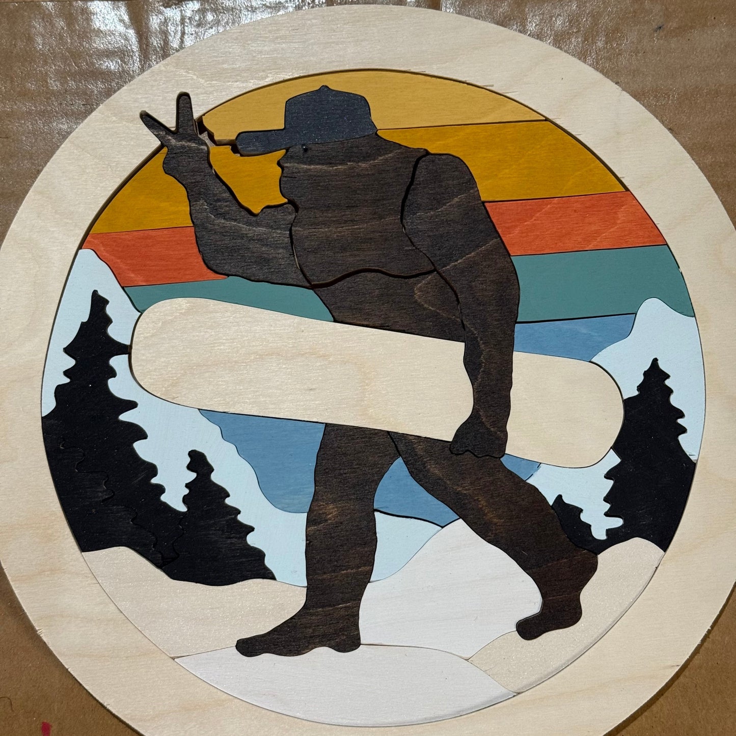 Wooden puzzle of bigfoot holding a snowboard with a mountain and sunset background.